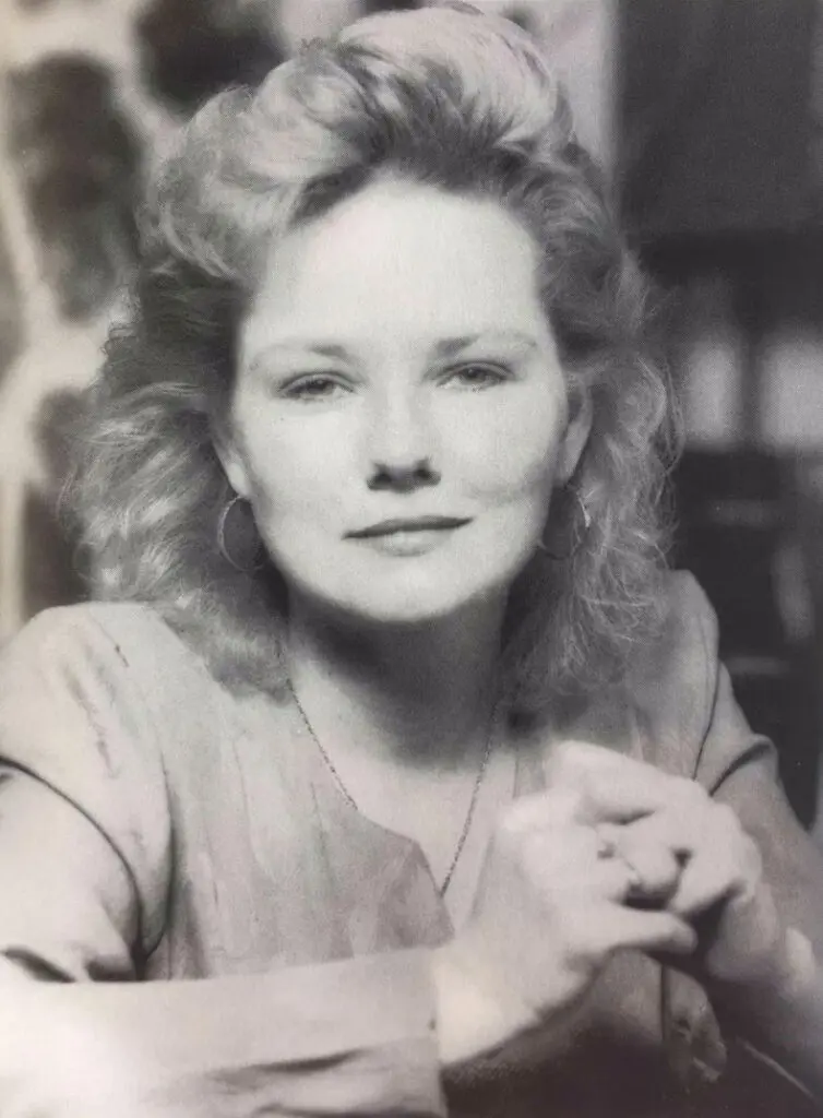 Black-and-white portrait of a woman with curly blonde hair, hoop earrings, and a subtle smile.