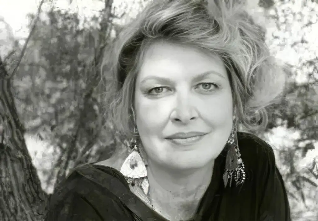 Black-and-white portrait of a woman outdoors, smiling softly, with blurred trees in the background.