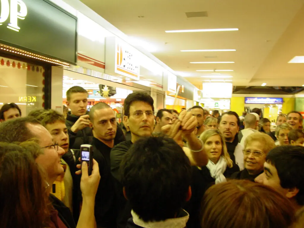Crowded mall aisle with many people standing close together in a busy store corridor.