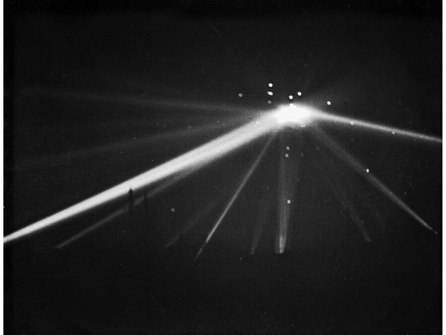 Battle-of-Los-Angeles-1942-LAT - UAPedia Black-and-white photo of multiple light beams radiating from a central bright point in the dark, forming a fan-like pattern.