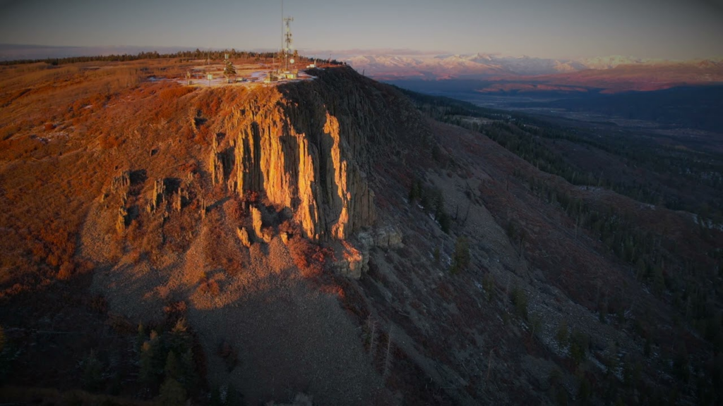 Rocky cliff face bathed in sunset light, with a communications facility and antennas on the summit coast-to-coast view.