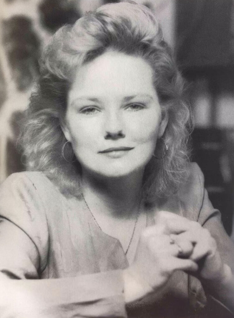 Black-and-white portrait of a woman with curly blonde hair, hoop earrings, and a subtle smile.