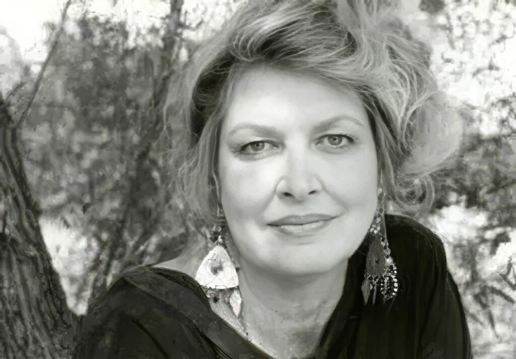 Black-and-white portrait of a woman outdoors, smiling softly, with blurred trees in the background.